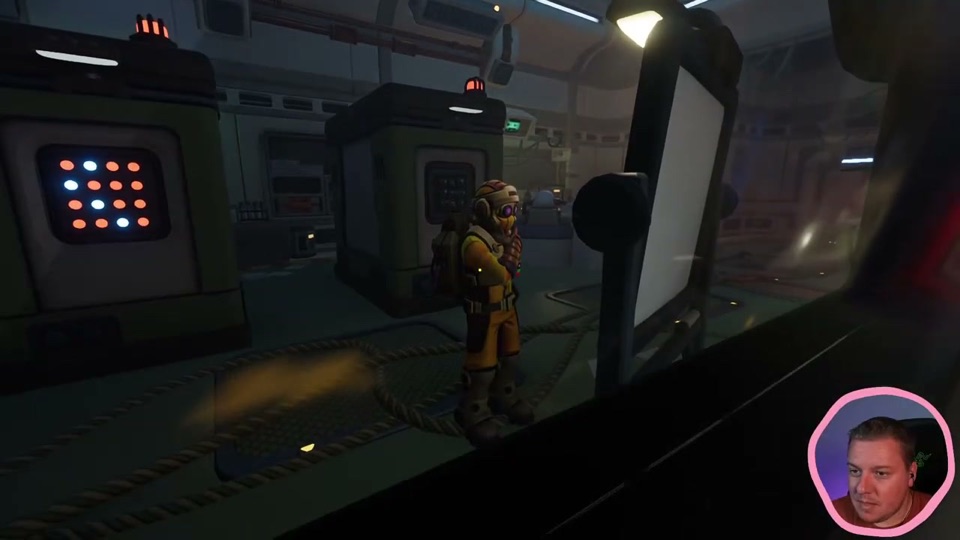 Seen from inside, a green lab cabinet with a 4x4 display of orange and white lights, and the yellow-suited partner standing in the lab